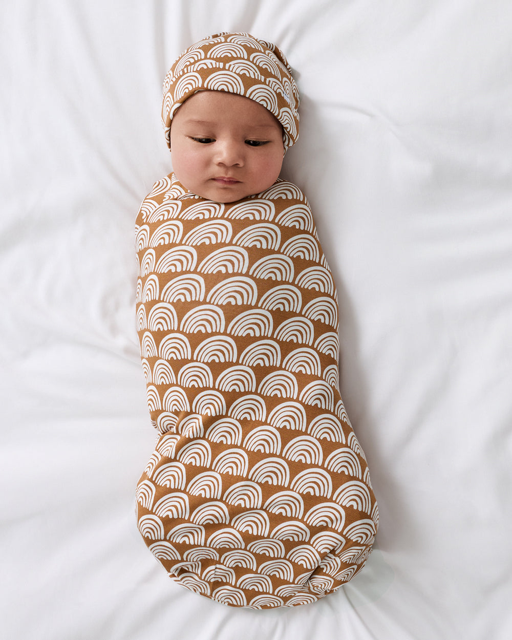 Aerial view of baby wrapped in the Rust Rainbows Swaddle & Beanie Set