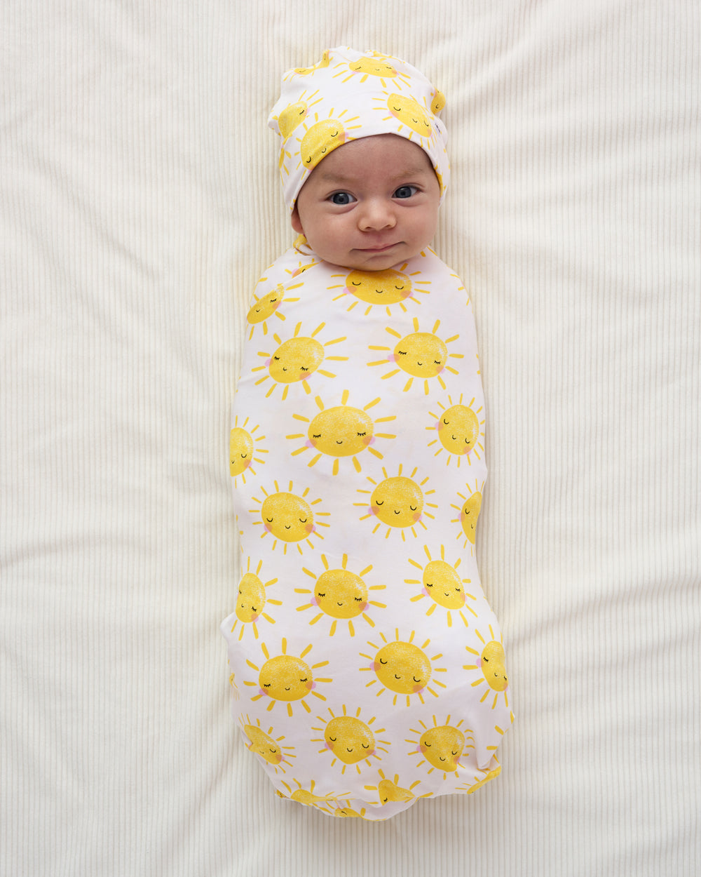 Baby swaddled in the gender neutral Sunshine Swaddle & Beanie Set