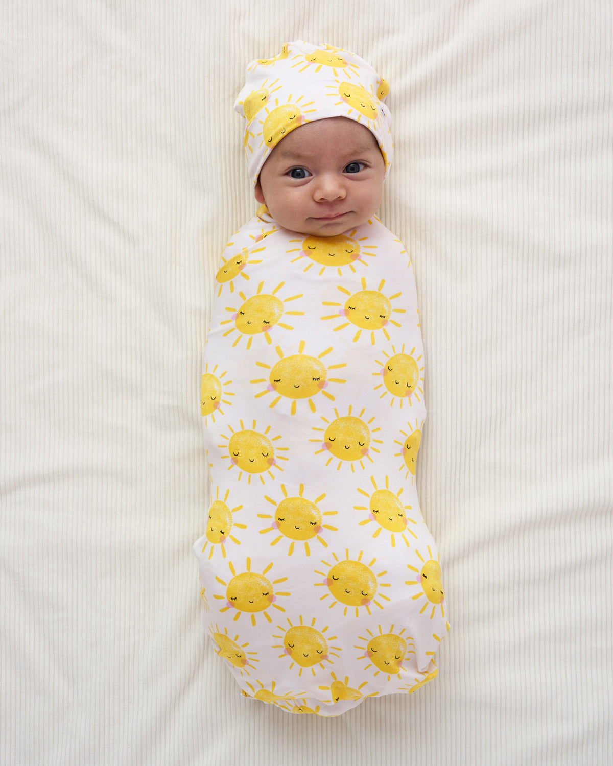 Baby swaddled in the gender neutral Sunshine Swaddle & Beanie Set