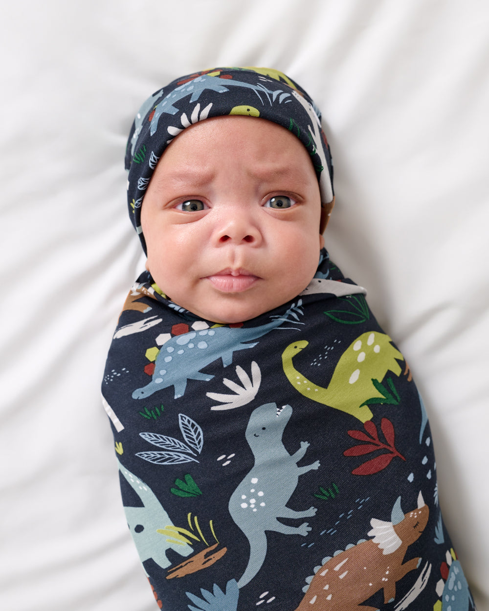 Close up of baby wrapped in the Navy Jurassic Jungle Swaddle & Beanie Set
