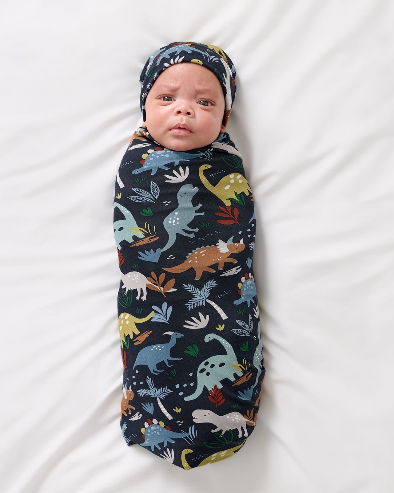 Aerial view of baby wearing the Navy Jurassic Jungle Swaddle & Beanie Set