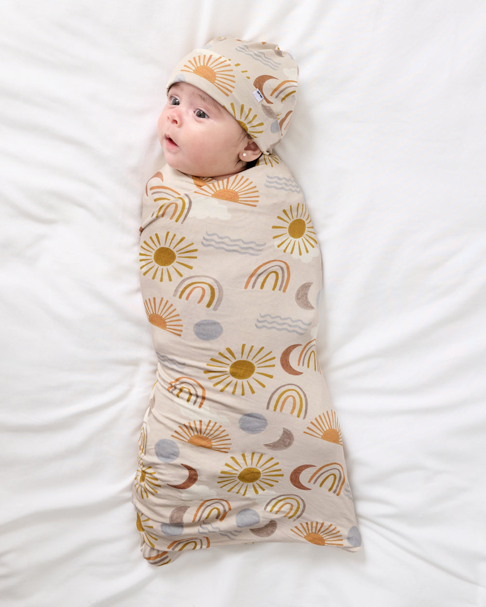 Aerial view of baby swaddled in the Desert Sunrise Swaddle & Beanie Set