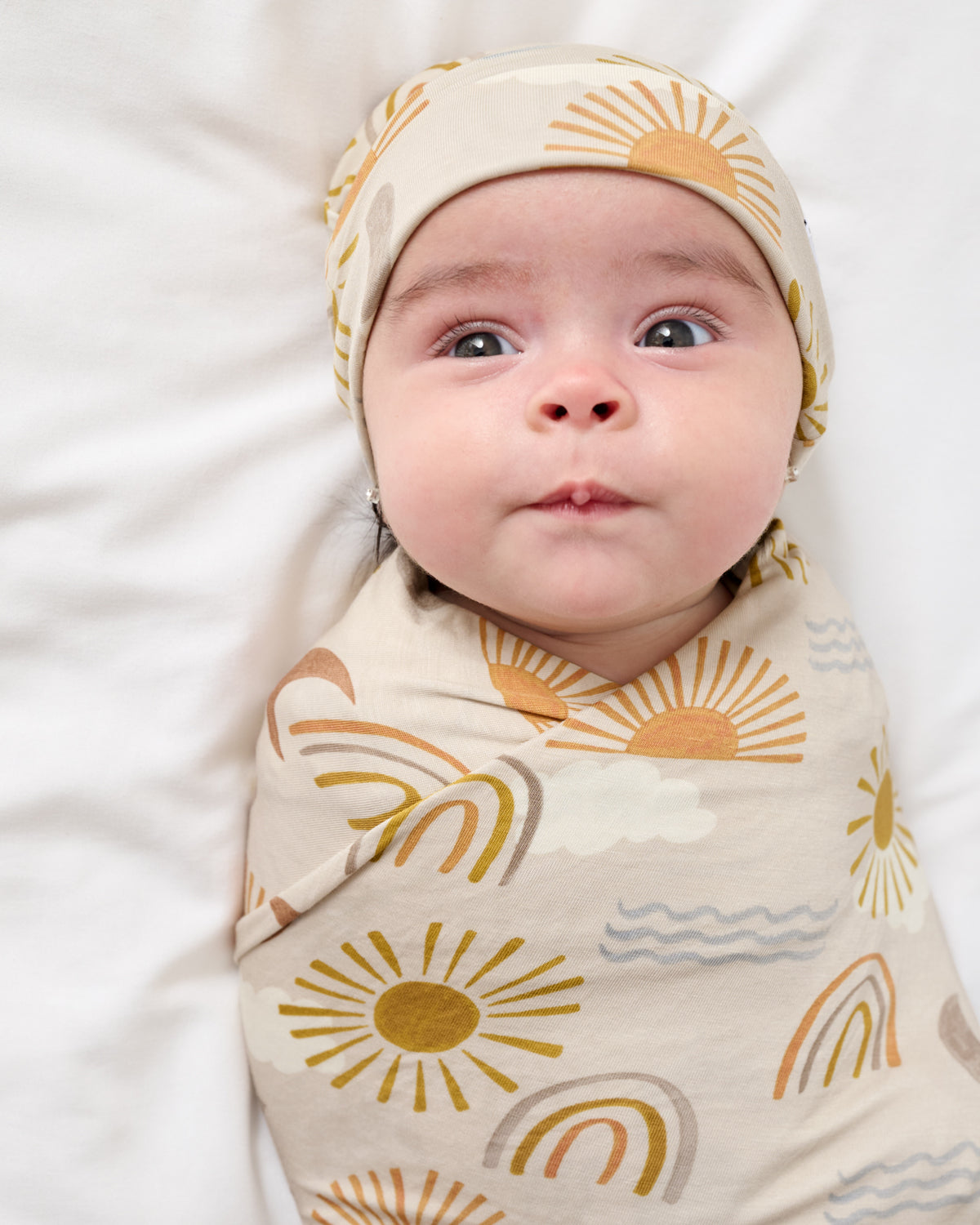 Close up of baby boy wrapped in the Desert Sunrise Swaddle & Beanie Set