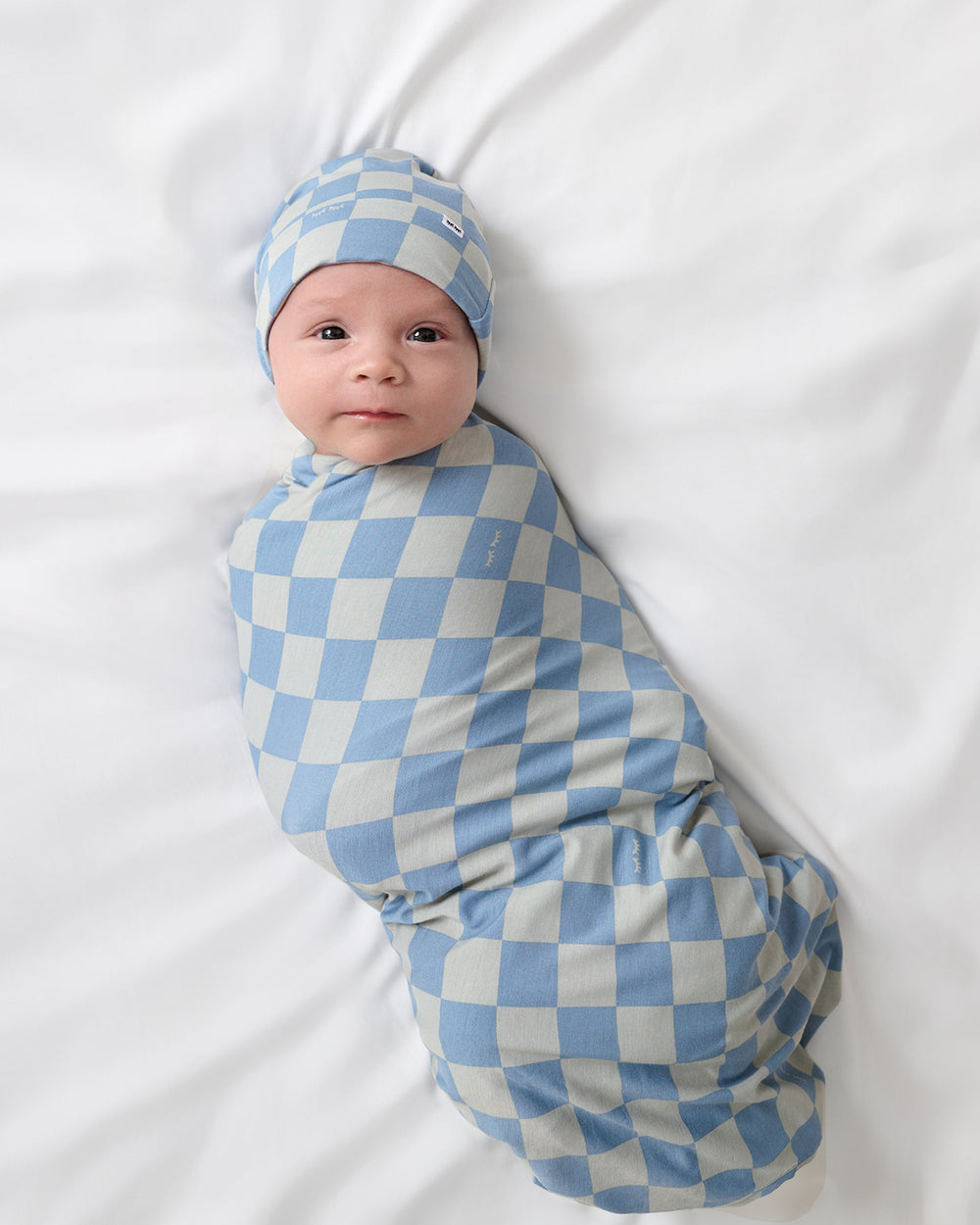Aerial view of baby wearing the Dusk Blue Checks Swaddle & Beanie Set