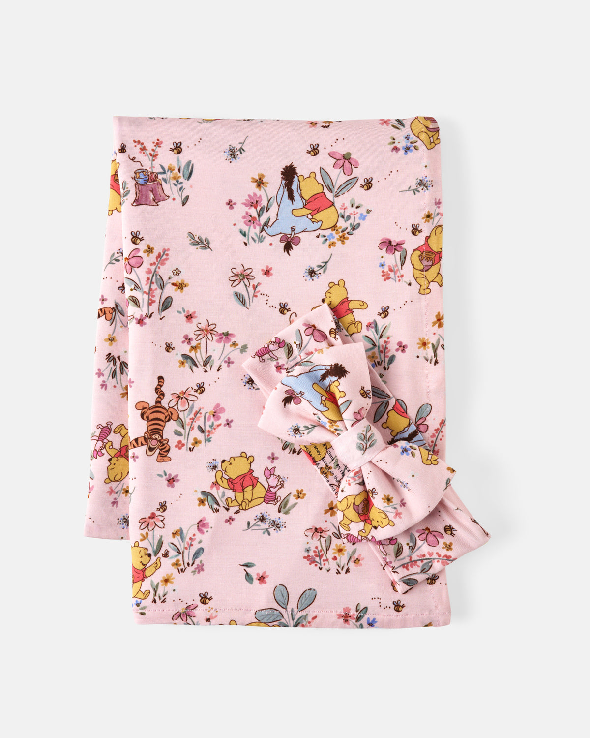 A folded pink blanket, featuring a colorful print of Winnie the Pooh, Tigger, and other Disney characters with small flowers and leaves, shown on a light gray background.