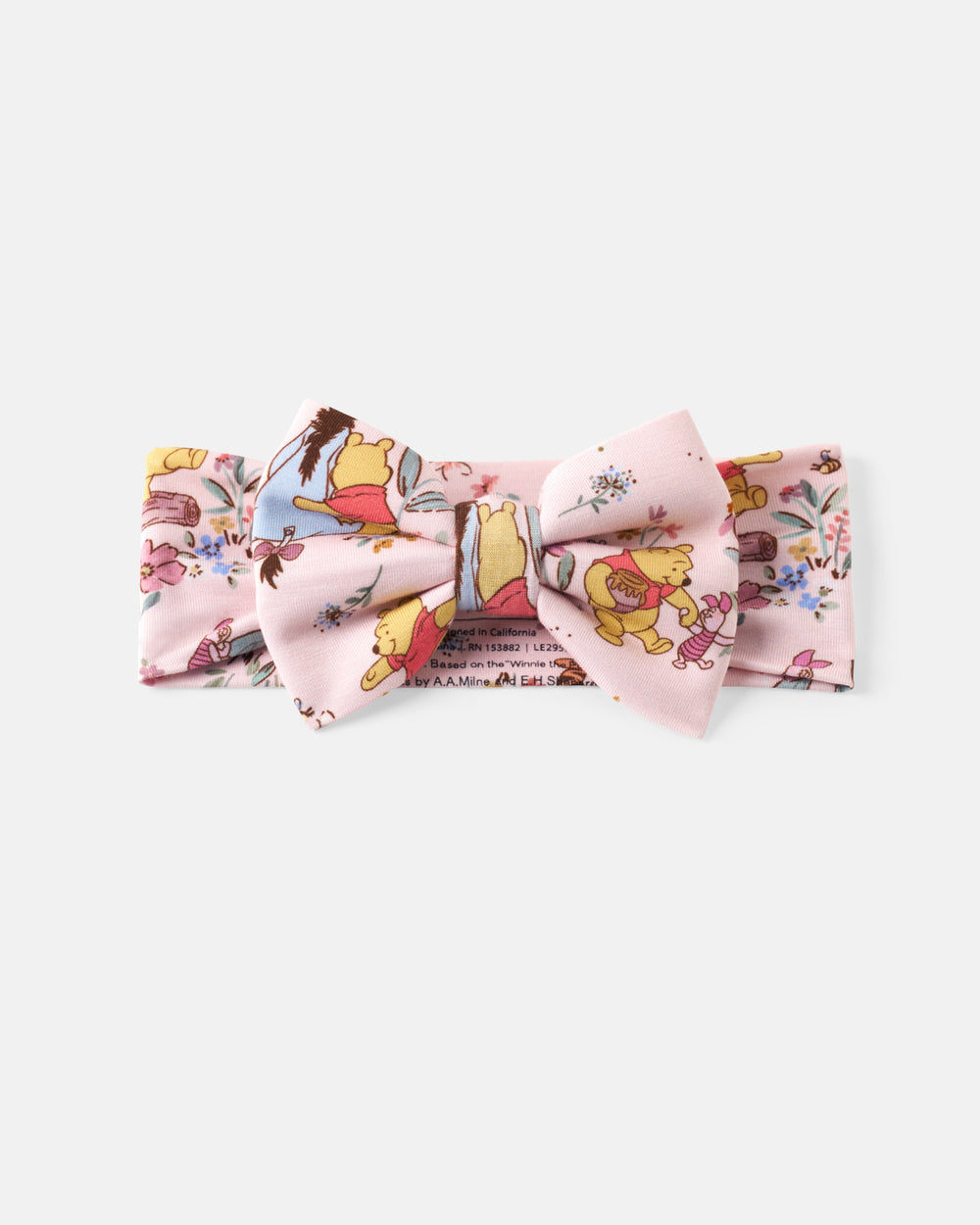 A light pink fabric accessory set featuring a bow tie and matching bandana with a whimsical cartoon character print, displayed on a clean light gray background.