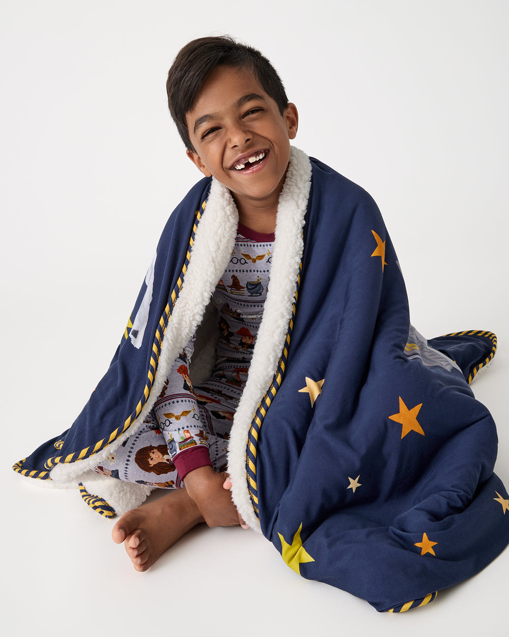 Sitting boy with the Harry Potter™ Spellbinding Studies Sherpa Large Cloud Blanket® over his shoulders