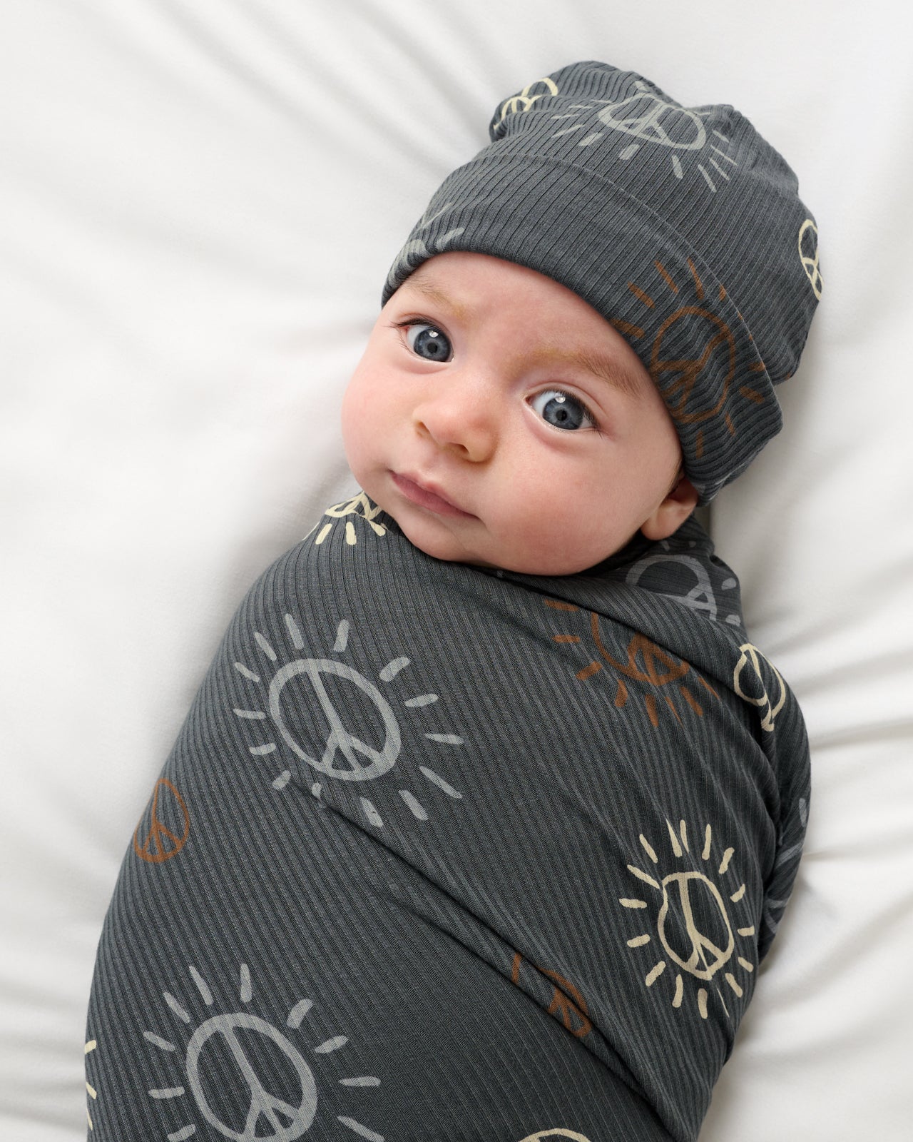 Close up of baby wearing the Peace & Love Ribbed Swaddle & Beanie Set