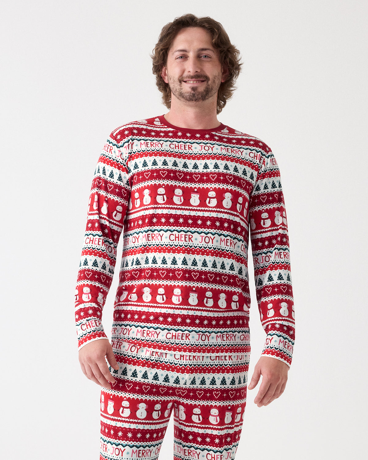 A man modeling a red, white, and green holiday-themed long-sleeve pajama set with a repeating pattern of snowmen, Christmas trees, hearts, and festive text, against a plain light gray background.