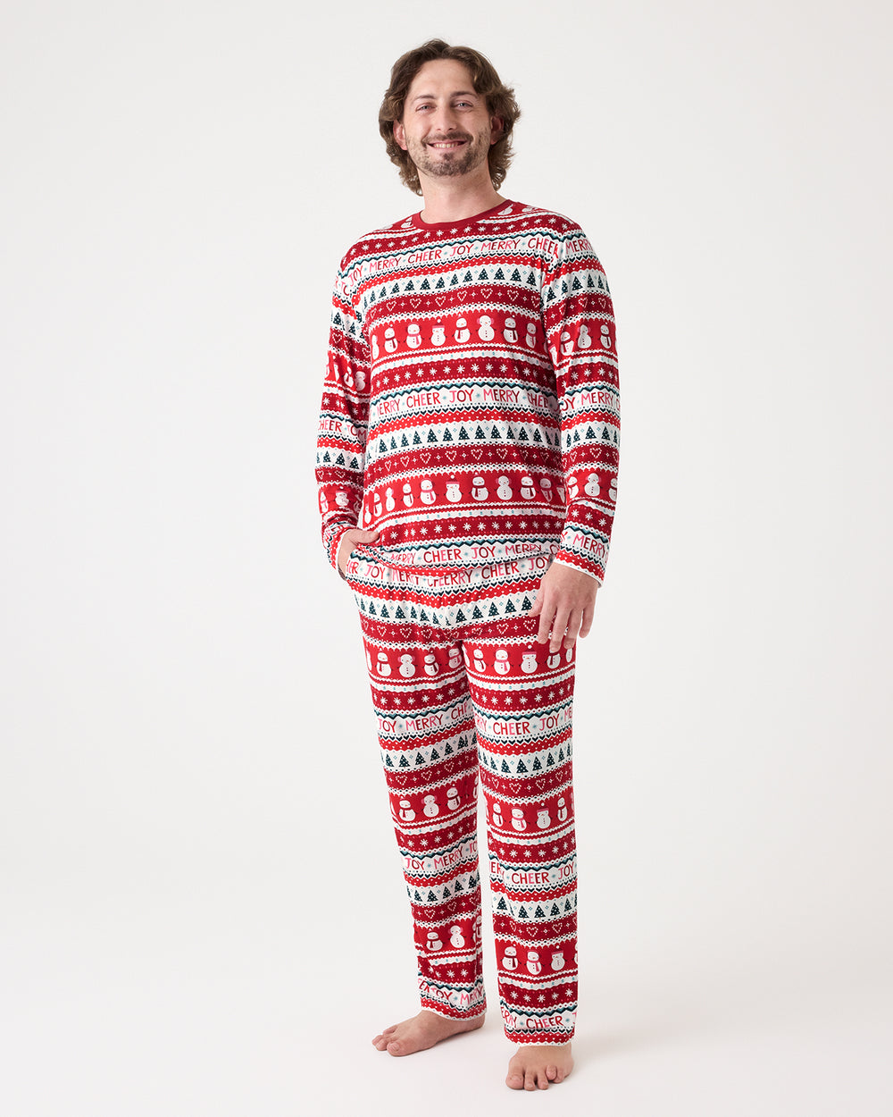 A man modeling a matching long-sleeve pajama set with a festive red, white, and black holiday pattern of snowmen, Christmas trees, and snowflakes, shot against a plain white studio background.