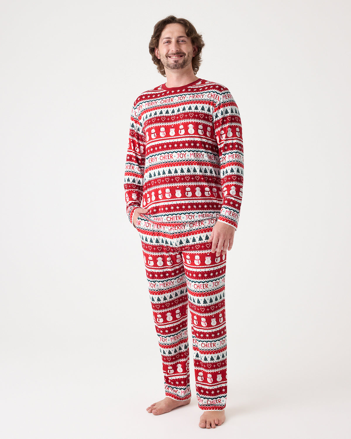 A man modeling a matching long-sleeve pajama set with a festive red, white, and black holiday pattern of snowmen, Christmas trees, and snowflakes, shot against a plain white studio background.