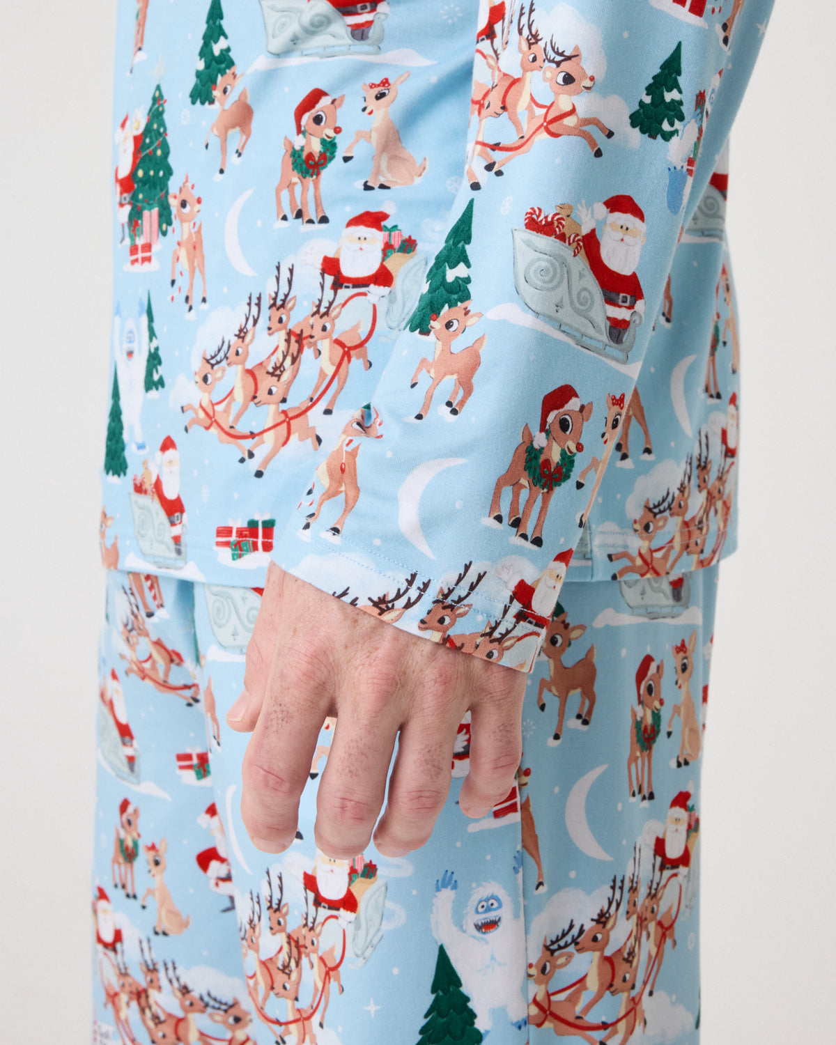 A close-up of a person wearing light blue pajama pants with a festive Christmas print featuring Santa Claus, reindeer, trees, and snowflakes.
