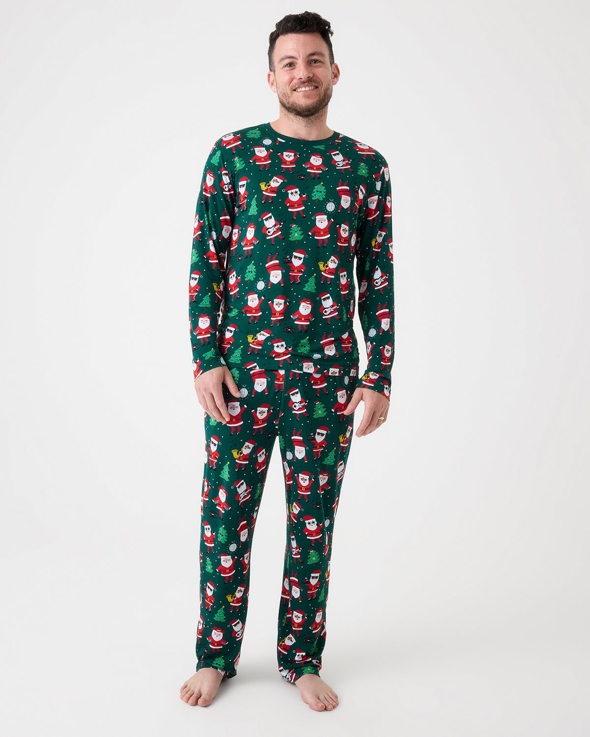 A man modeling a matching long-sleeve pajama set with a green Christmas Santa pattern, standing against a plain white studio background.