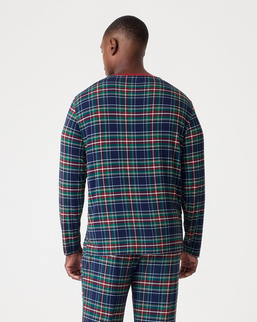A man viewed from behind wearing a matching long-sleeve plaid pajama top and pants set in navy blue with red and green stripes, standing against a plain white studio background.