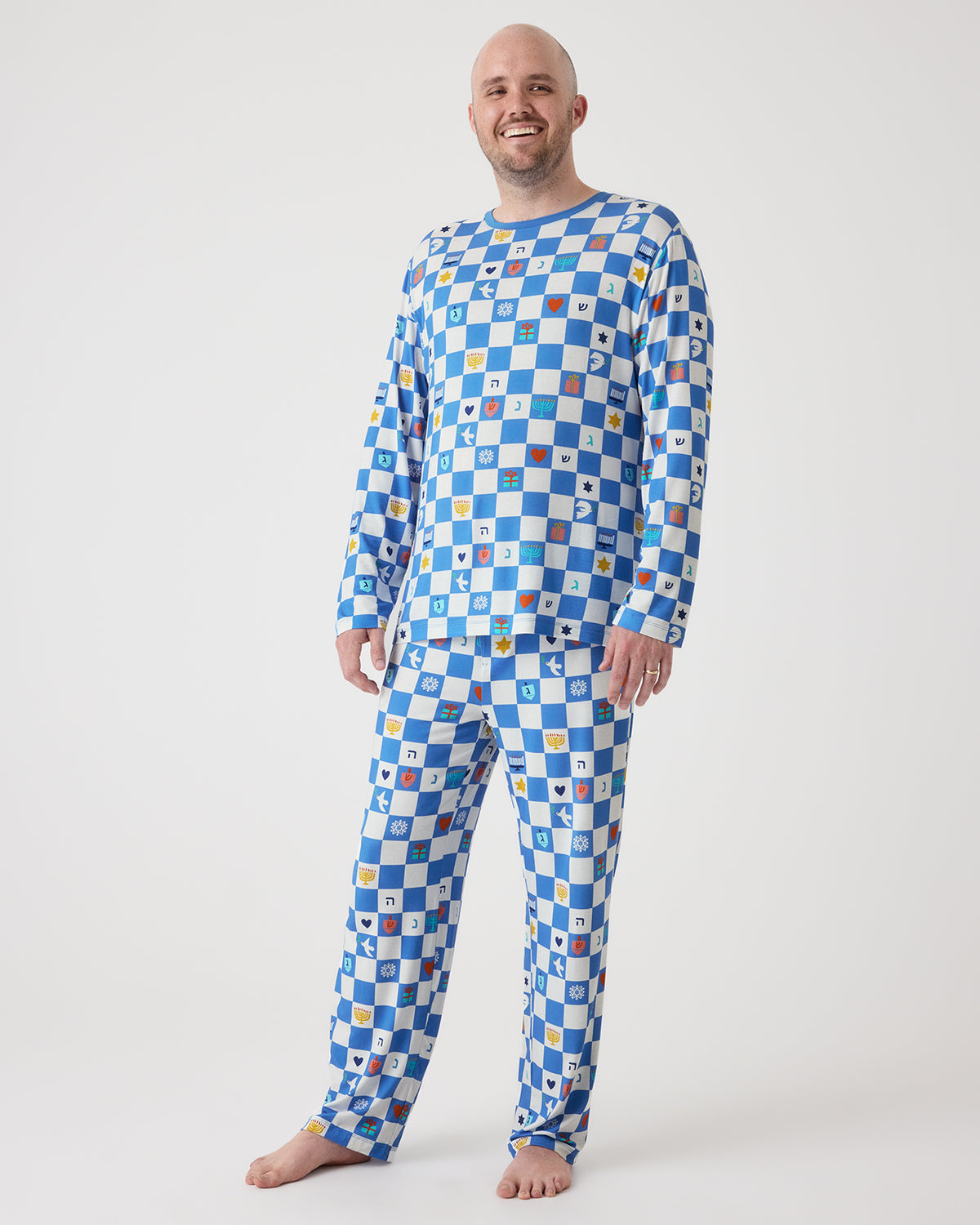 A bald man wearing a long-sleeve pajama set with a blue and white checkerboard pattern, standing against a plain light gray studio background.