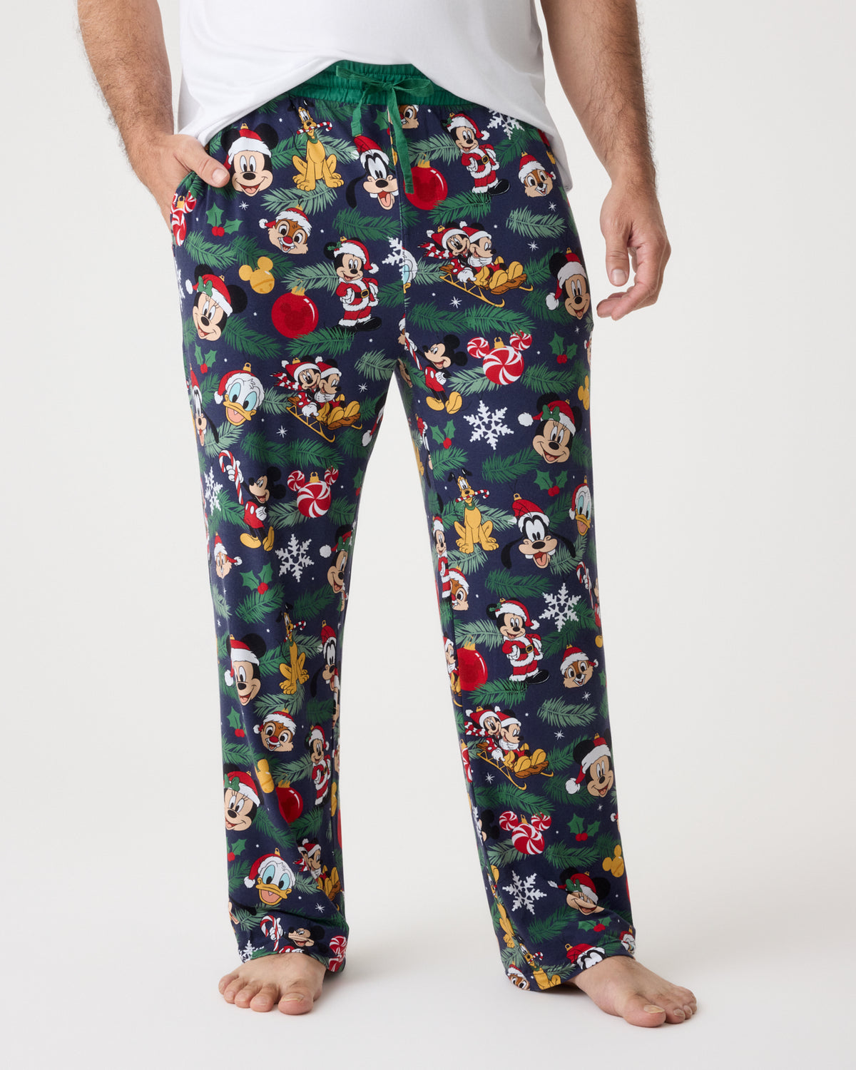 Men's Christmas-themed lounge pants featuring an all-over print of Disney characters like Mickey Mouse, Minnie Mouse, Donald Duck, and Goofy in holiday attire, shown on a model against a white studio background.