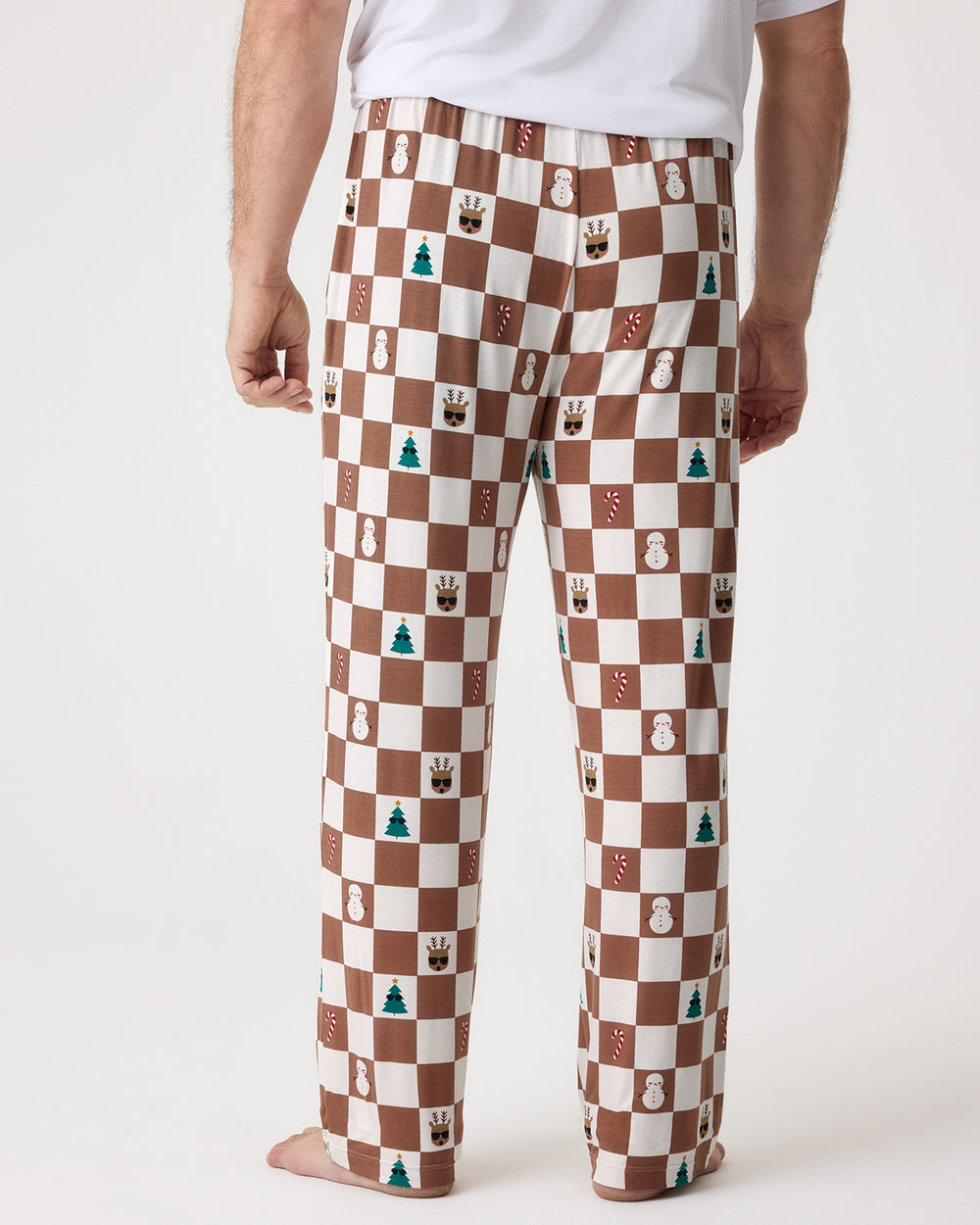 A person shown from the waist down wearing patterned brown and cream checkerboard pajama pants with small holiday-themed icons, against a plain light background.