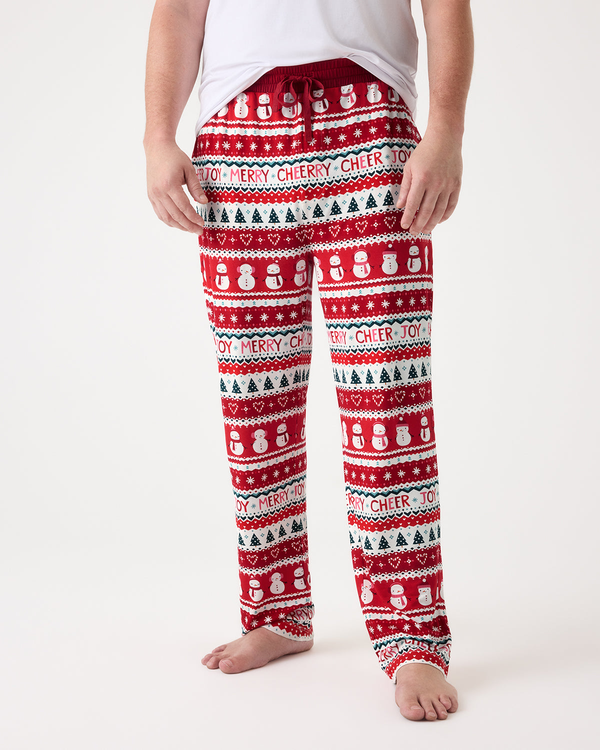 A person wearing red holiday PJ pants with a white and green Christmas pattern, shown from the waist down against a plain white studio background.