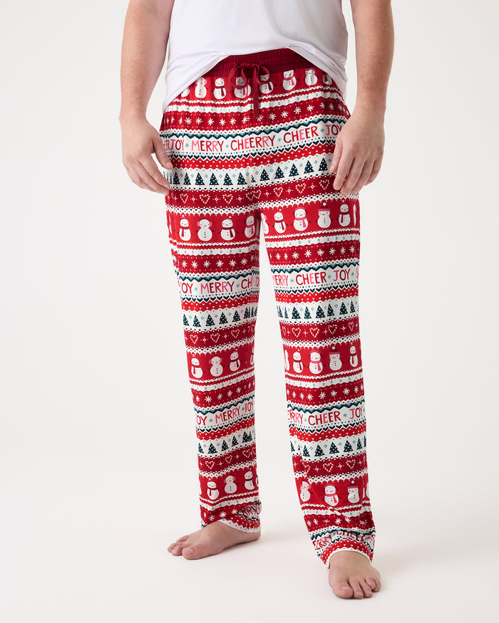 A person wearing red holiday PJ pants with a white and green Christmas pattern, shown from the waist down against a plain white studio background.