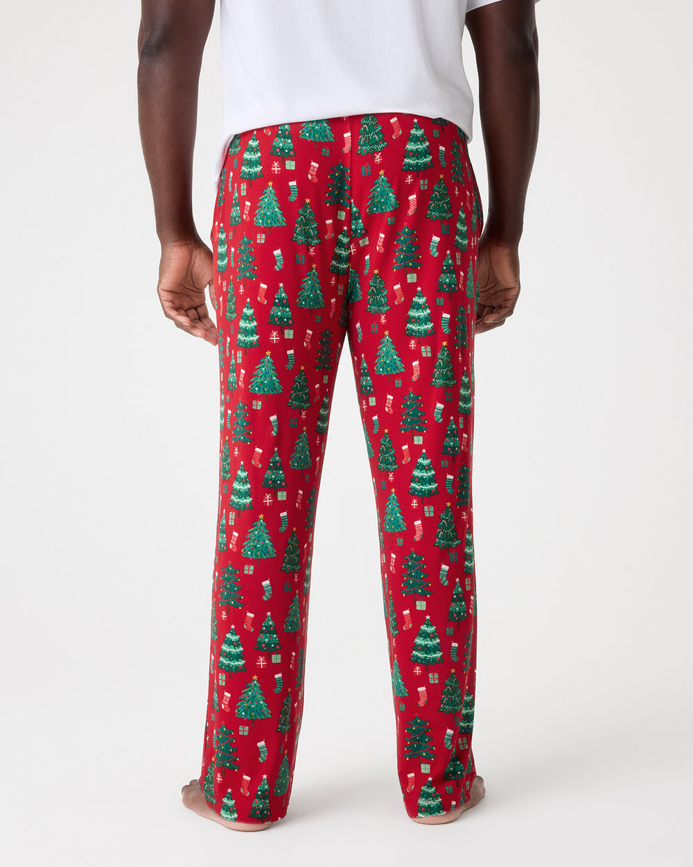 A person shown from the back wearing red pajama pants with a green Christmas tree pattern, standing against a light gray studio background.