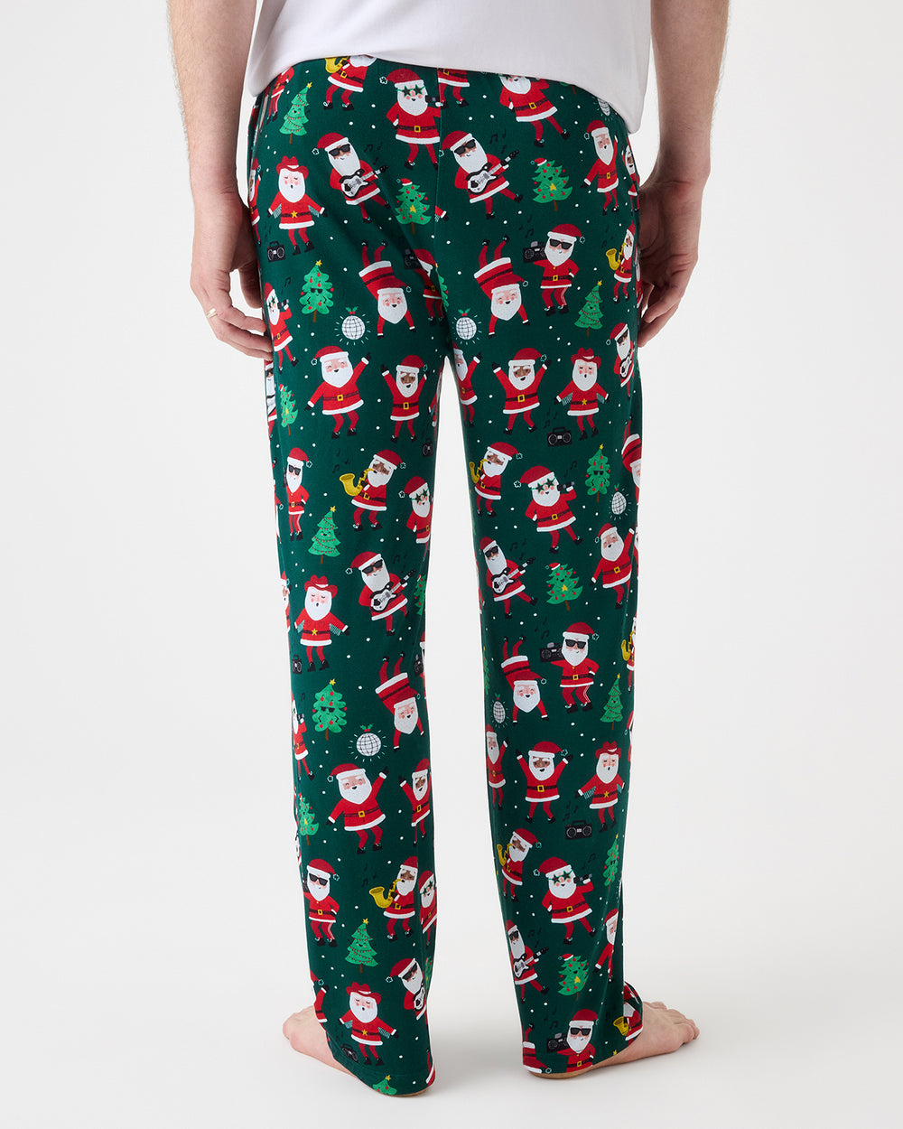 A person shown from the back wearing dark green Christmas pajama pants with an all-over Santa Claus print, photographed against a clean light gray studio background.