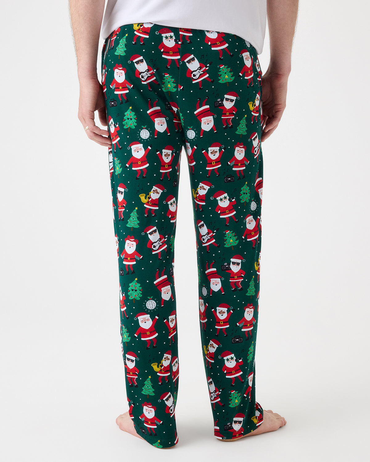 A person shown from the back wearing dark green Christmas pajama pants with an all-over Santa Claus print, photographed against a clean light gray studio background.