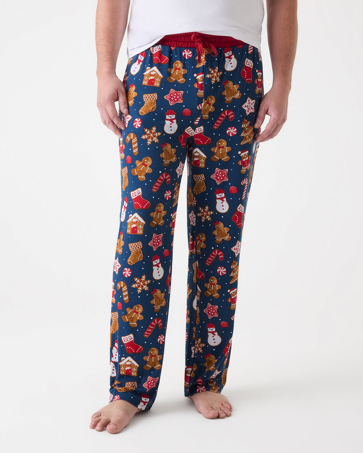 A person wearing navy blue holiday-themed lounge pants with a gingerbread, snowman, and candy cane print, paired with a white top, shown against a plain white studio background.