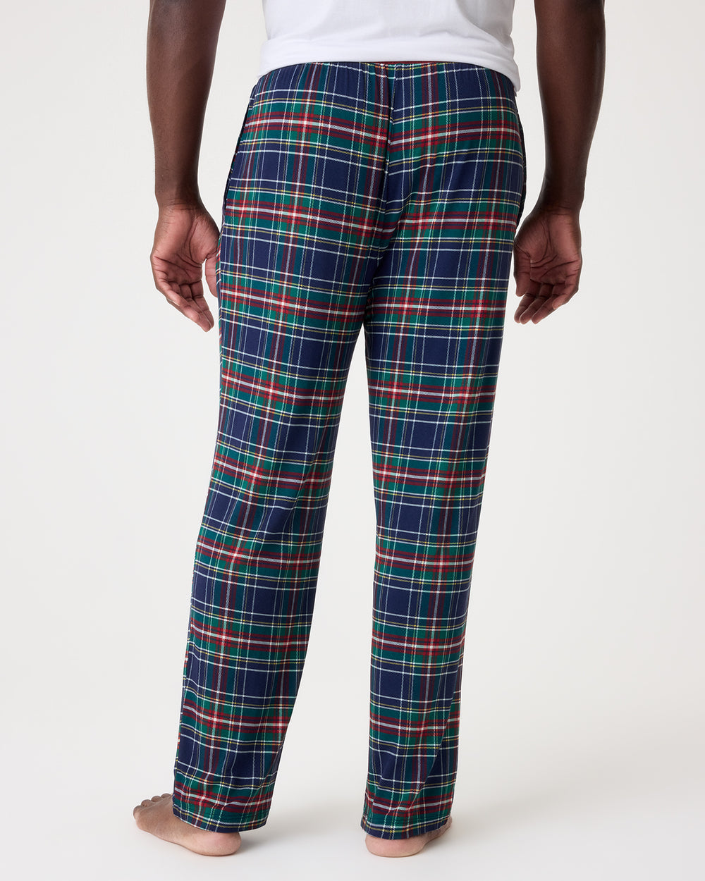A person shown from the back wearing plaid pajama pants in navy blue with red, green, and white lines, standing barefoot against a plain light background.