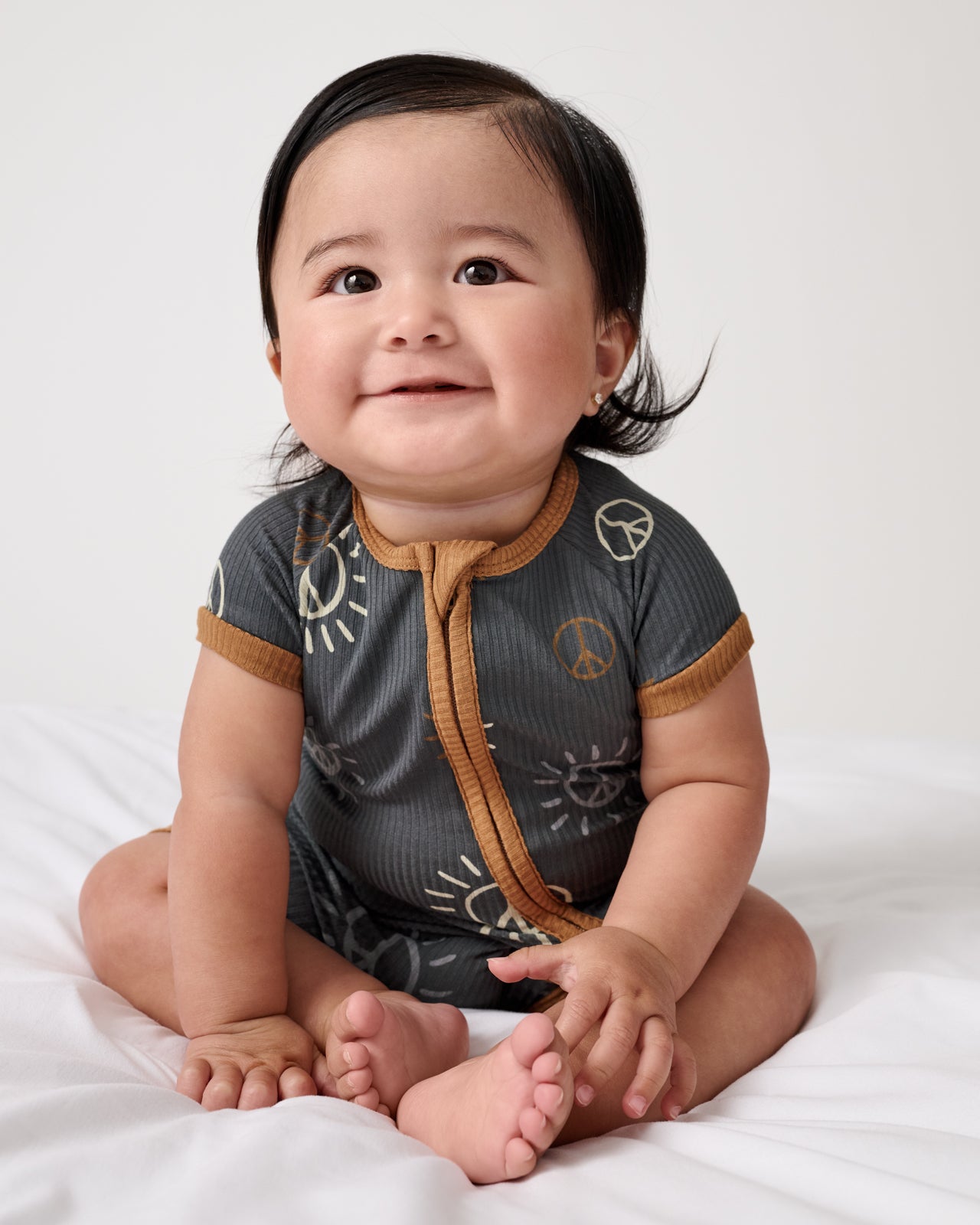 Sitting baby wearing the Peace & Love Ribbed Shorty Zippy