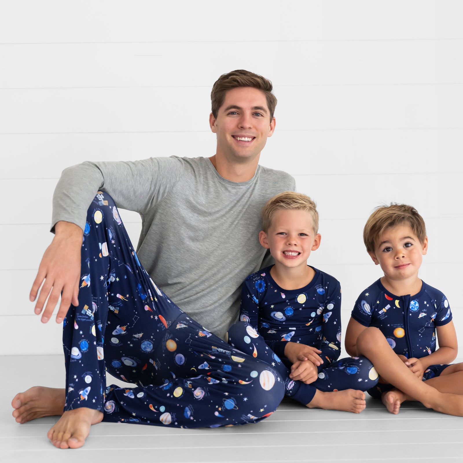 Father and his two children wearing matching Through My Telescope pjs in mens, and children's two piece and shorty zippy styles. Dad is pairing his pants with a men's Heather Gray pj top