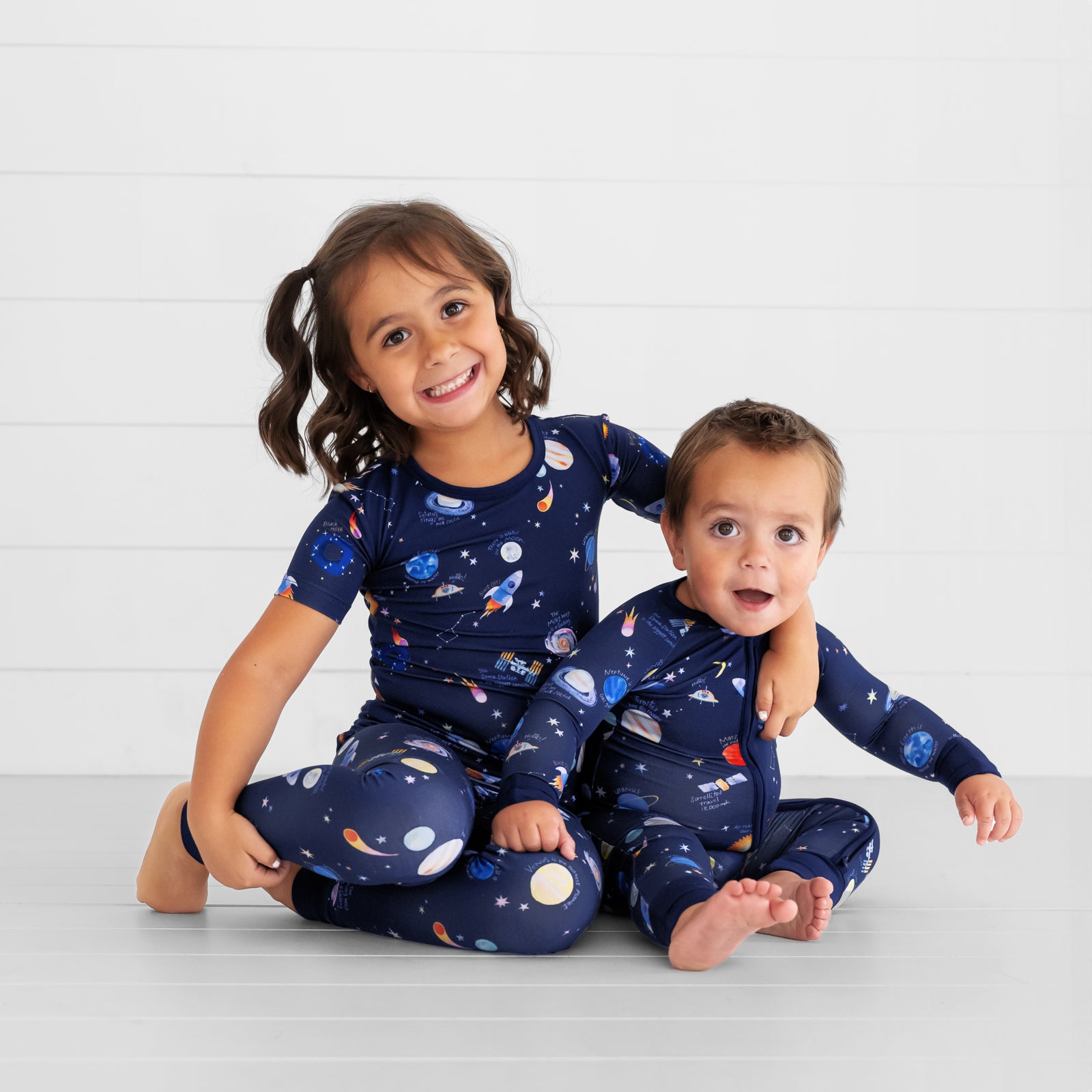 Image of two children sitting together wearing matching Through My Telescope pj sets in zippy and two piece short sleeve styles