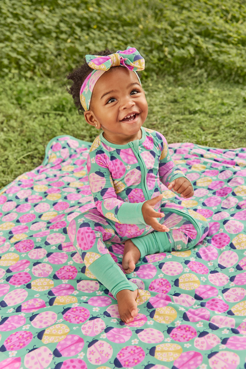 Baby sitting on the Ladybug Meadow Large Cloud Blanket® with grass in the background