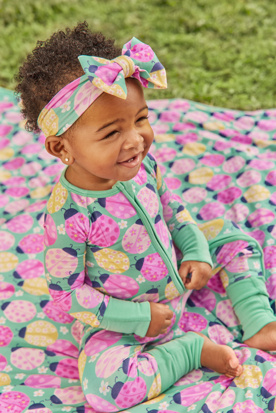 Child sitting on a Ladybug Meadow printed blanket wearing the matching Luxe Bow Headband
