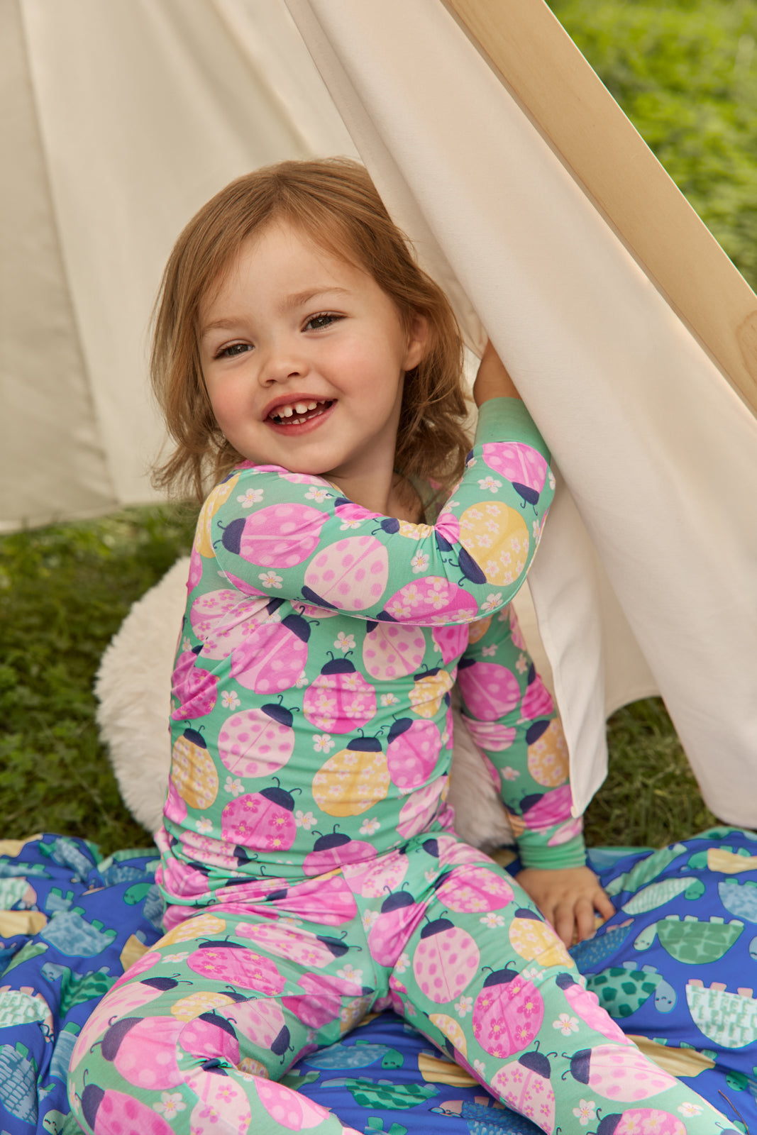 Child sitting in a white tent wearing the Ladybug Meadow Two-Piece Pajama Set