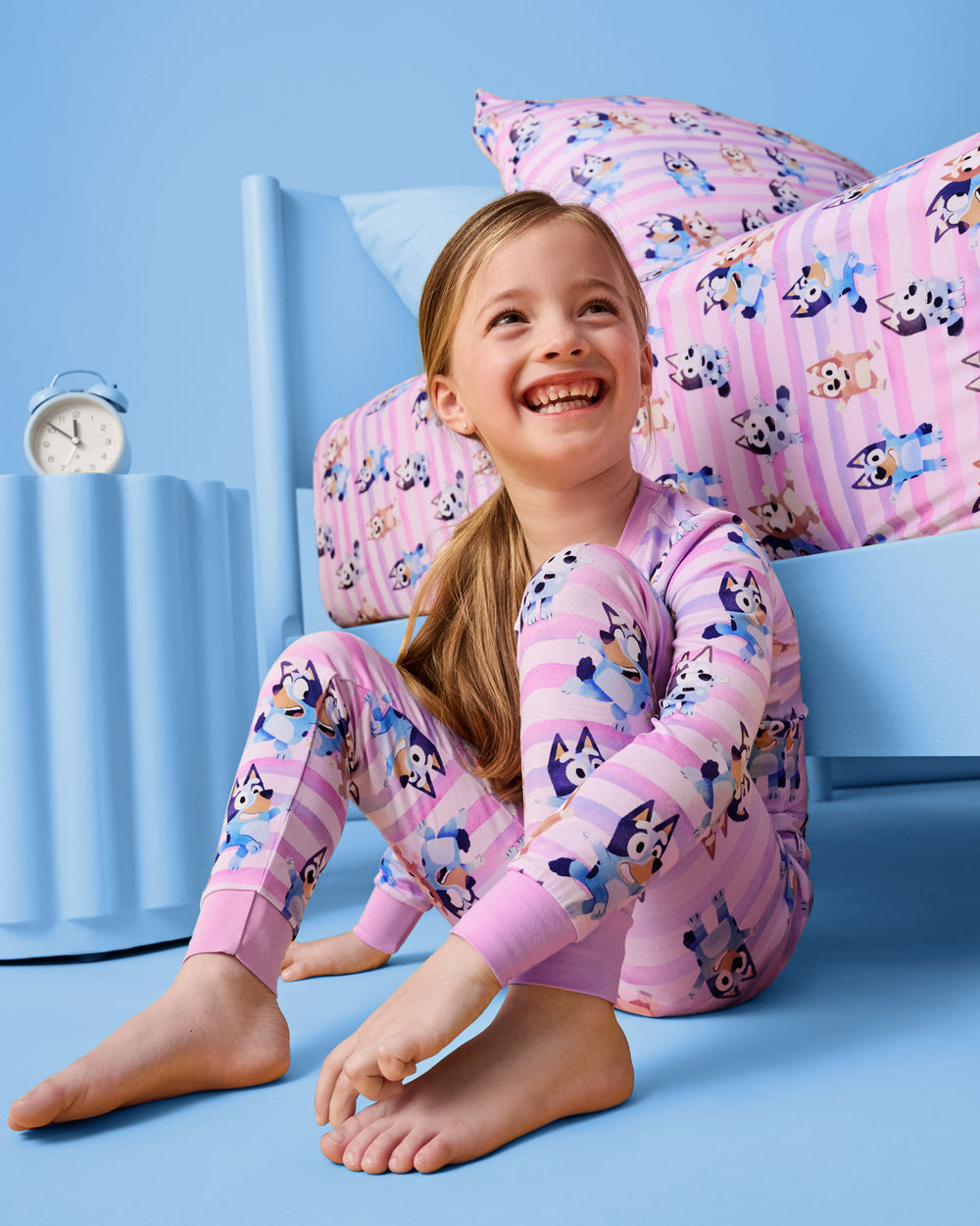 Girl wearing the Pink Bluey Dance All Day Two-Piece Pajama Set with a blue bedroom set behind her