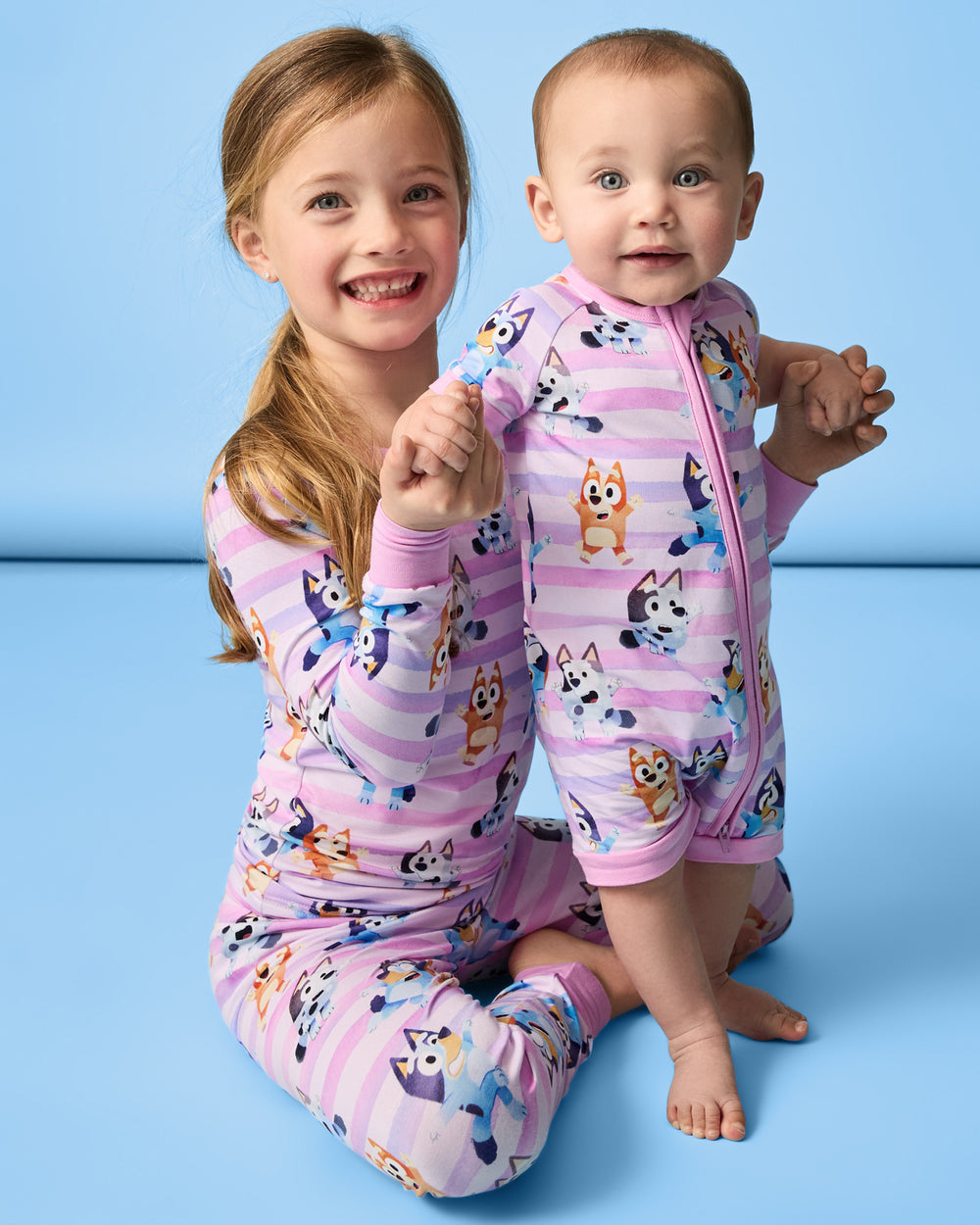 Two children wearing matching Pink Bluey Dance All Day Pajamas on a blue back drop