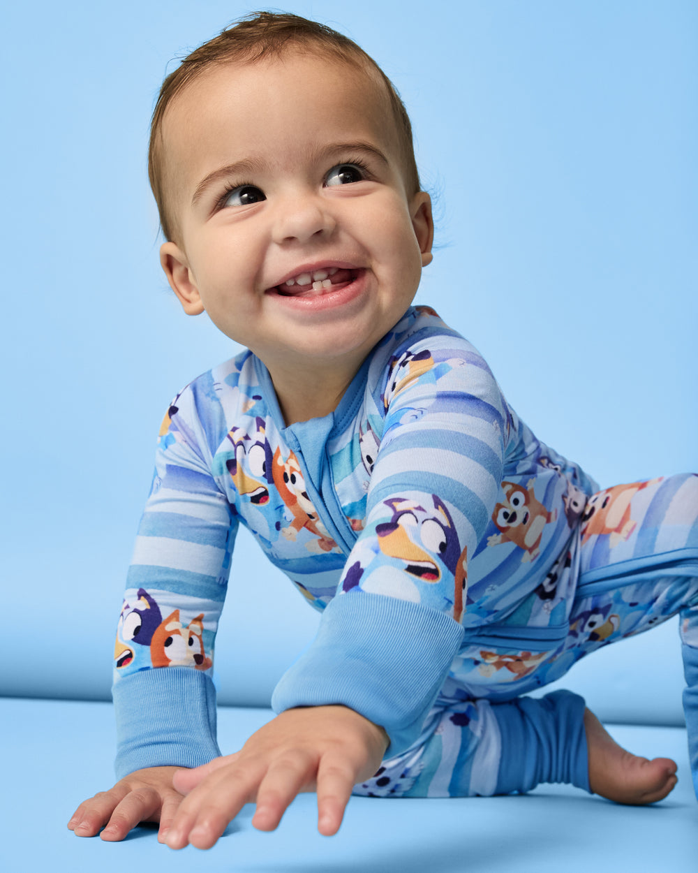 Crawling baby wearing the Bluey Dance All Day Zippy on a blue background