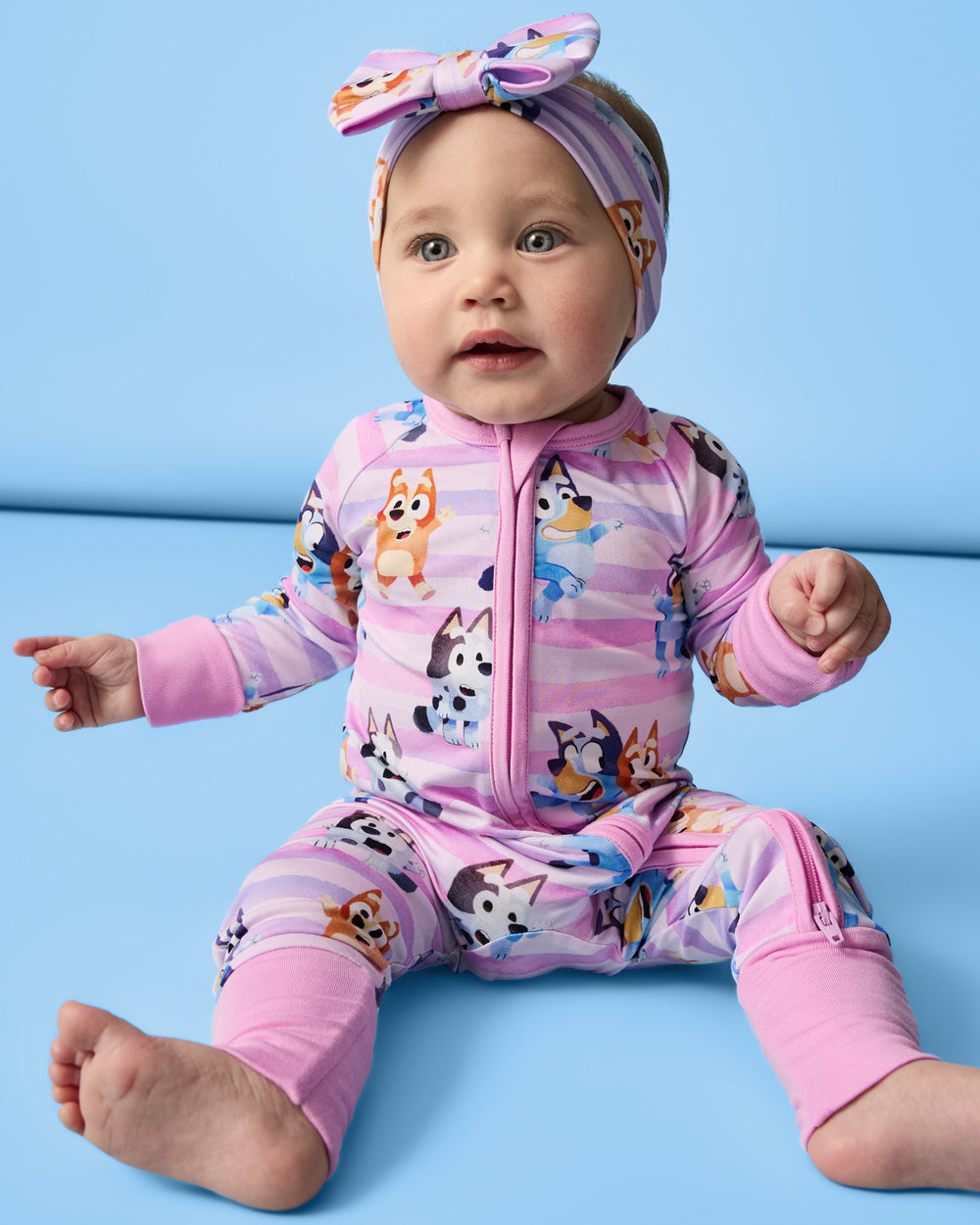 Sitting baby wearing the Pink Bluey Dance All Day Zippy and Luxe Bow on a blue background