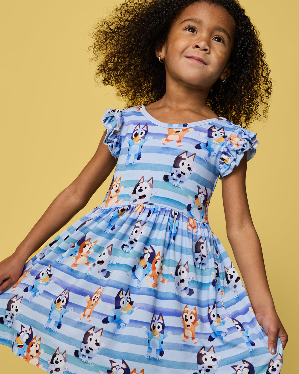 Close up of girl wearing the Bluey Dance All Day Flutter Skater Dress on a yellow back drop