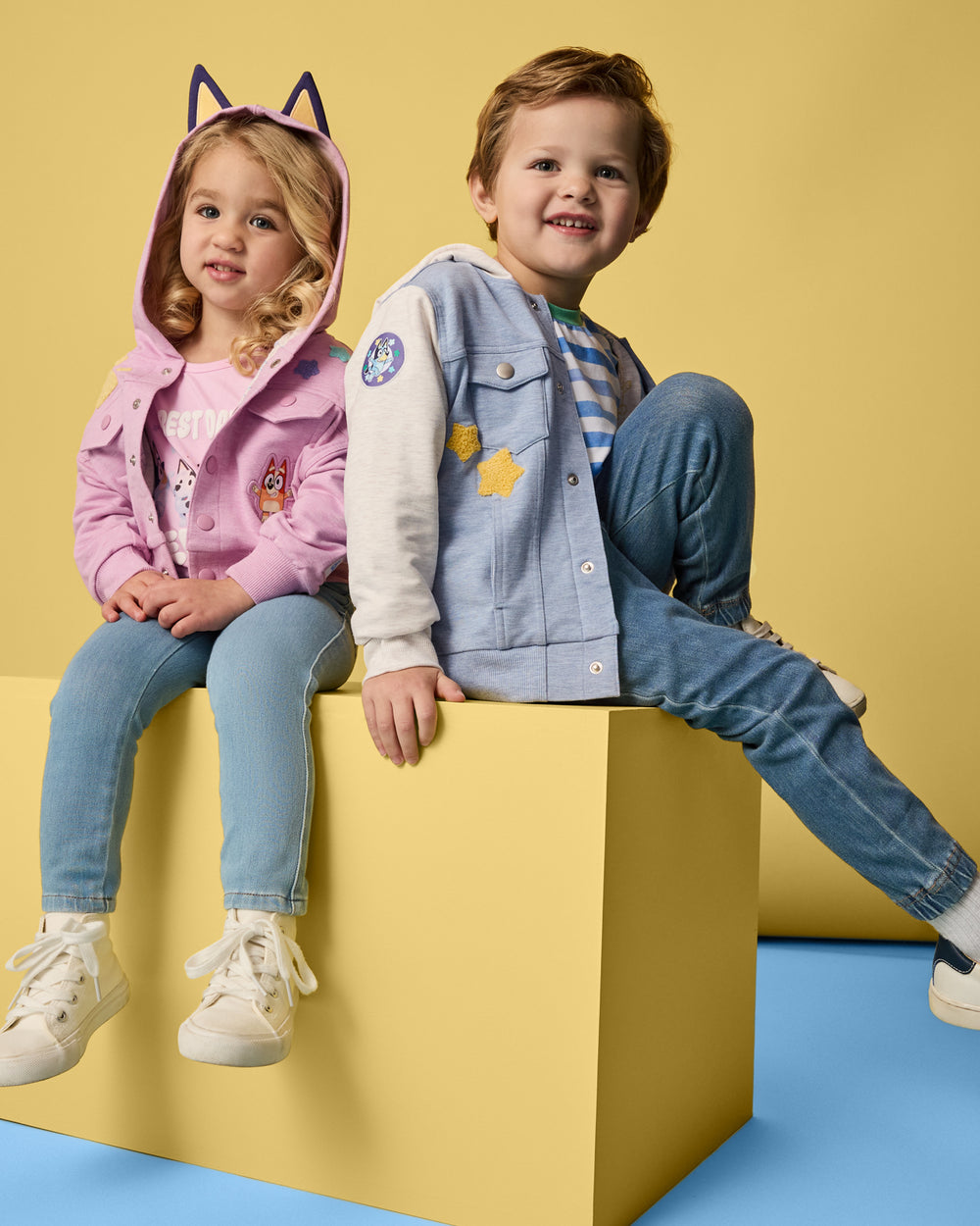 Two kids wearing Pink and Blue Bluey Trucker Jackets on  yellow background
