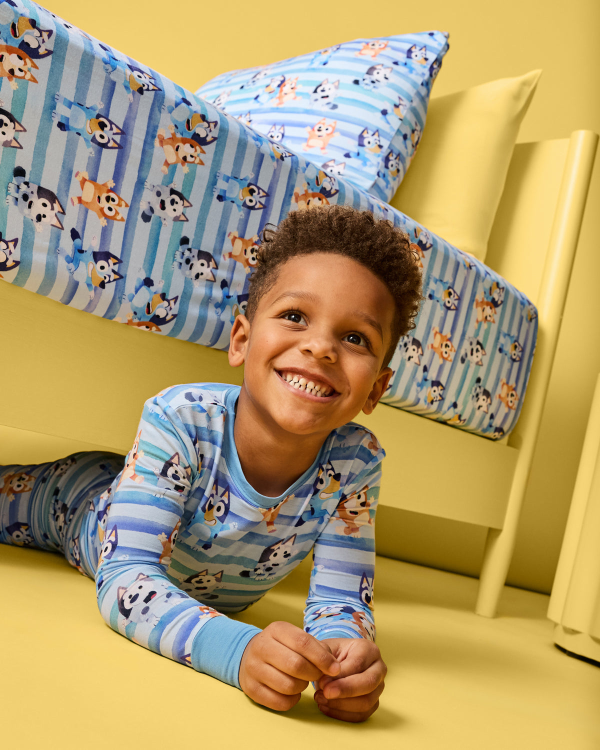 Child laying on a yellow surface wearing the Bluey Dance All Day Two-Piece Pajama Set
