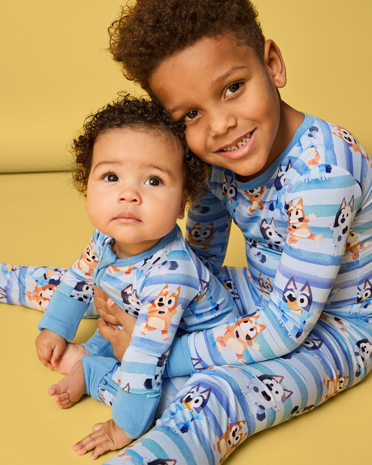 Two children sitting on a yellow surface wearing matching Bluey Dance All Day Kids Pajamas