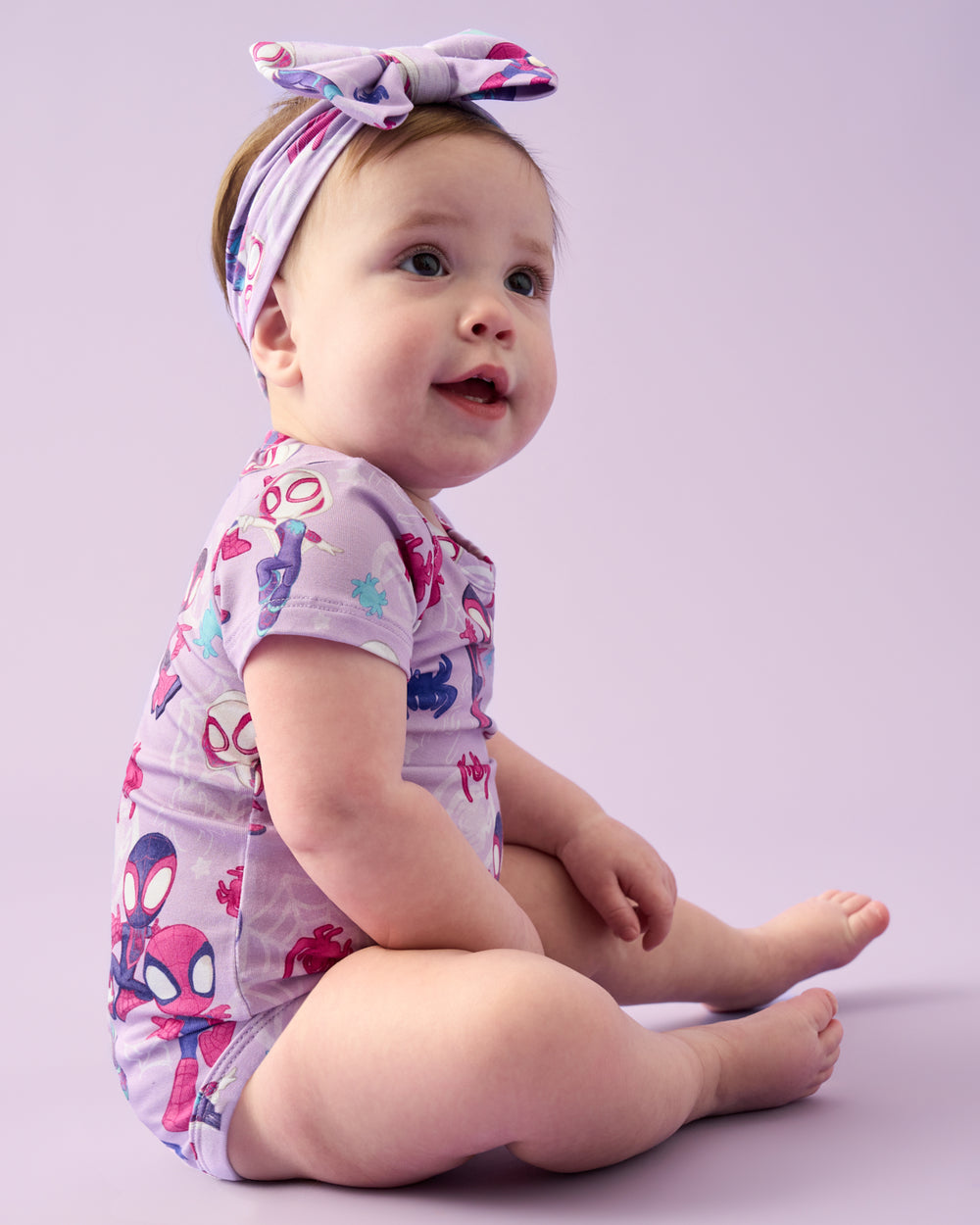 Sitting baby wearing the Spidey & Friends Tiny Webs Short Sleeve Bodysuit and Luxe Bow Headband