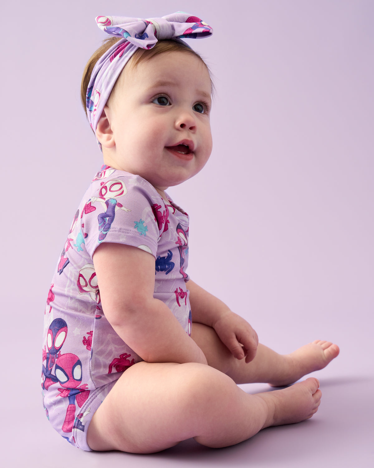 Sitting baby wearing the Spidey & Friends Tiny Webs Short Sleeve Bodysuit and Luxe Bow Headband