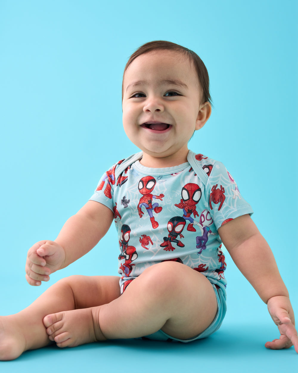 Sitting baby wearing the Spidey & Friends Tiny Webs Short Sleeve Bodysuit on a blue back drop