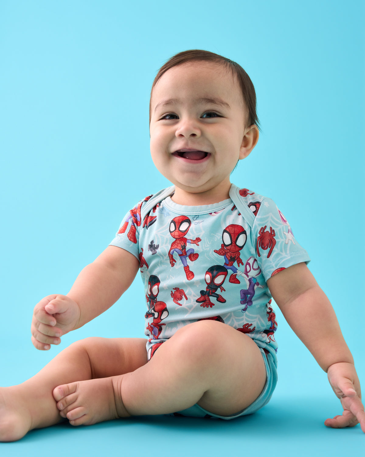 Sitting baby wearing the Spidey & Friends Tiny Webs Short Sleeve Bodysuit on a blue back drop
