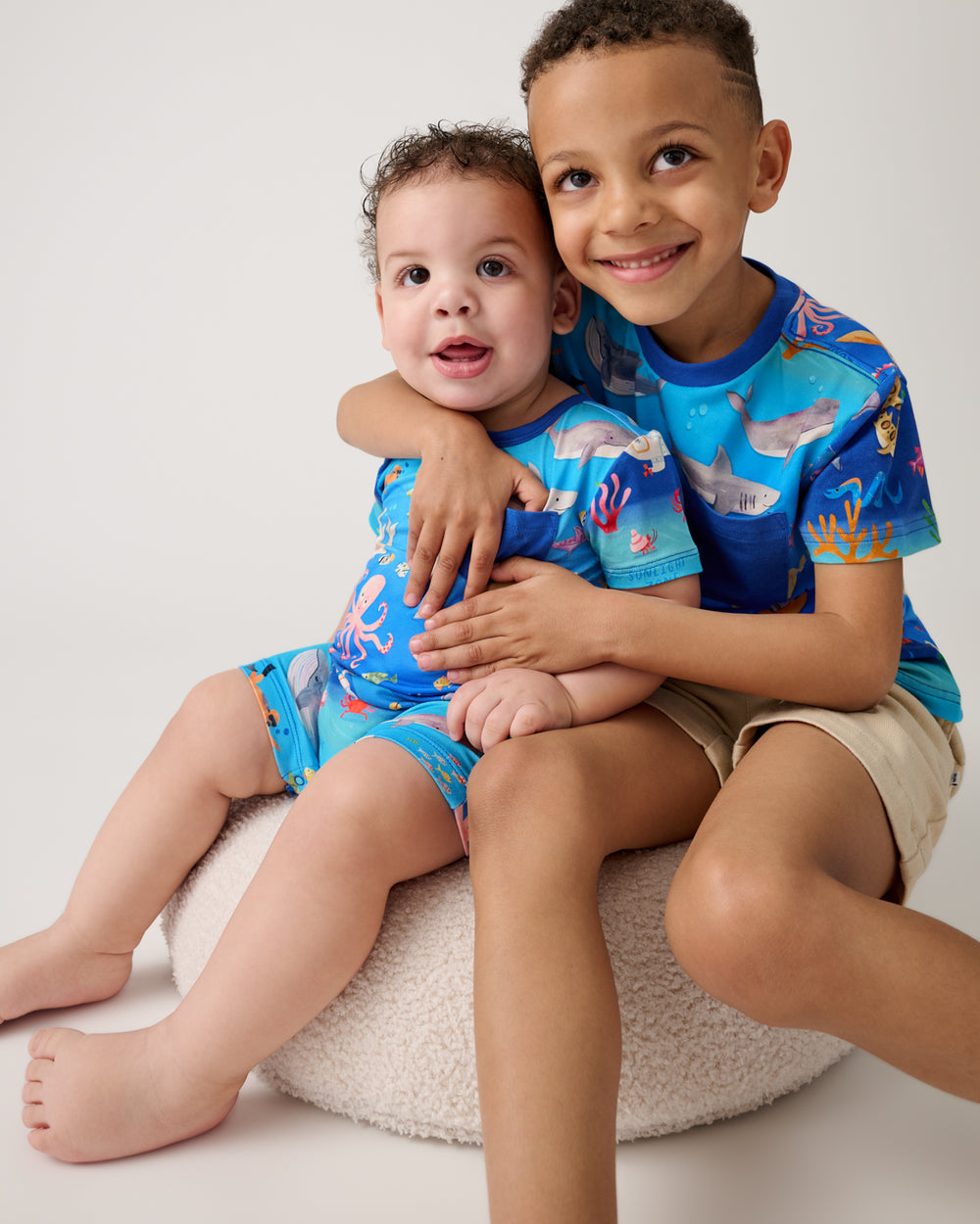 Two children sitting on a white ottoman wearing matching Underwater Discovery styles