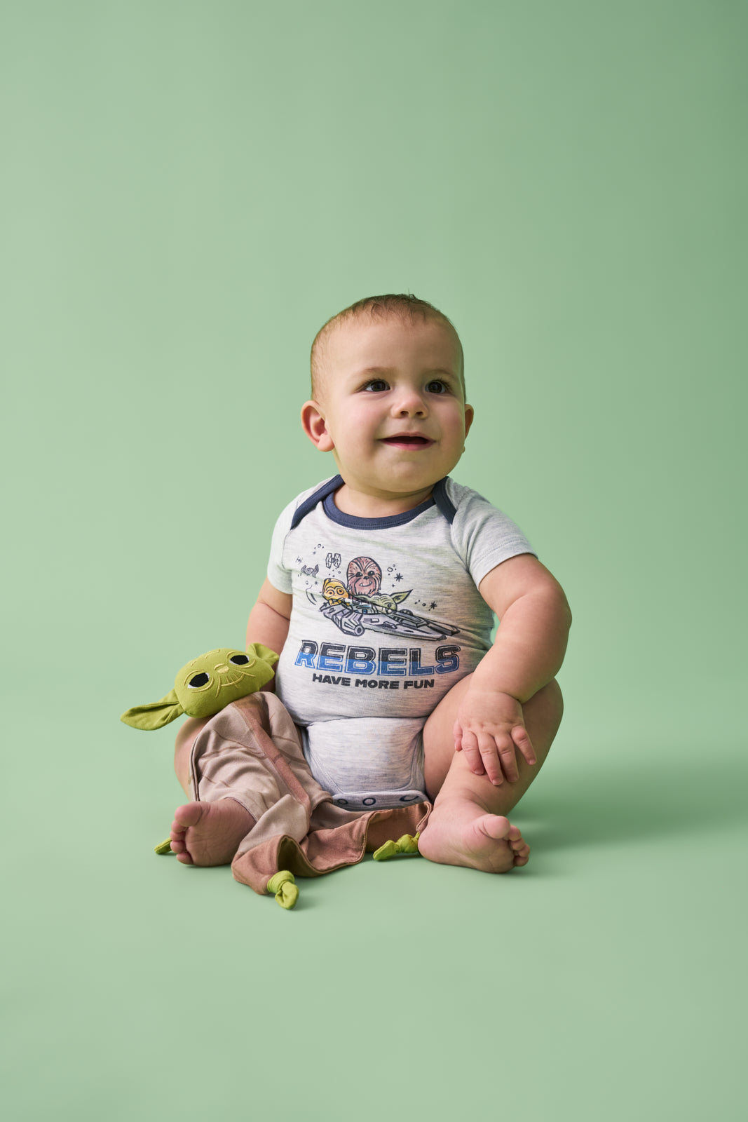 Baby wearing the Star Wars Little Rebels Short Sleeve Bodysuit sitting with the Star Wars Yoda Lovey