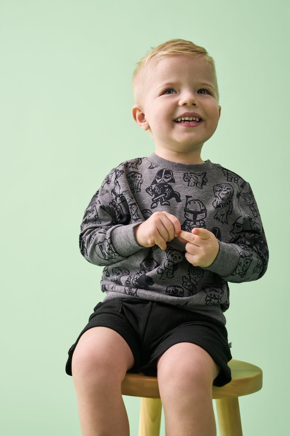 Boy sitting on a wooden stool wearing the Star Wars Far, Far, Away Friends Crewneck Sweatshirt