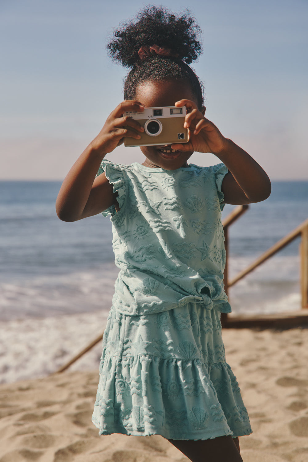Girl at the beach wearing the Coastal Rays Bow Front Flutter Top and Skirt